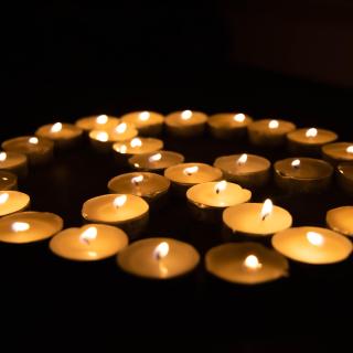 About 20 small lit tea lights are arranged, in the dark, in a peace symbol.
