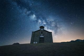 A stone church stands silhouetted against a night sky in which the Milky Way is visible.